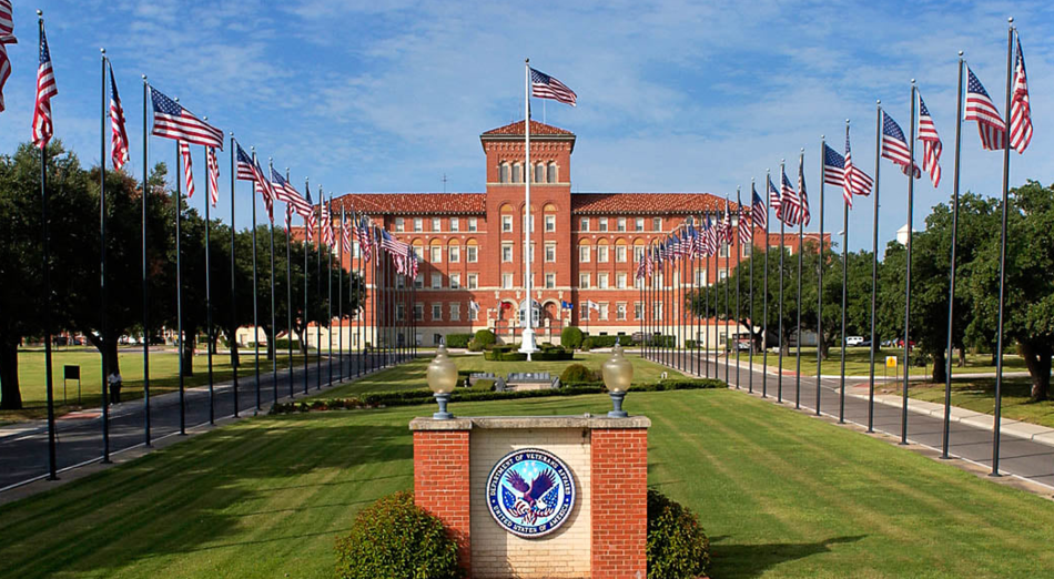 photo of the Central Texas Veterans Health Care System campus, with the building in the distance across a field of flag poles flying the American flag