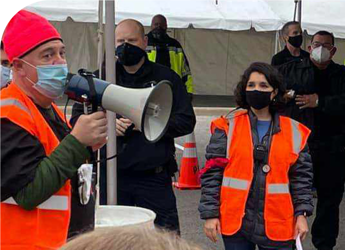 photo of Toby Hatton with a bullhorn and orange vest, speaking to a crowd of masked emergency personnel