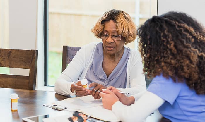 a patient and nurse discuss medication at the table at the patient's home