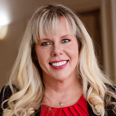 Candice-Smith-nm26 - Texas Hospital Association Smiling woman with long blonde hair and bangs, wearing a red blouse and black blazer, indoors.