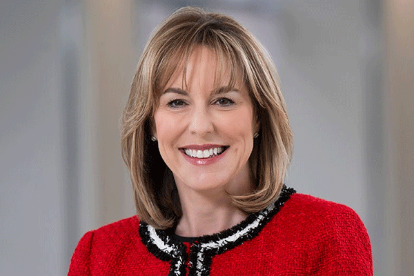 Portrait of a smiling woman with shoulder-length blonde hair wearing a red jacket.