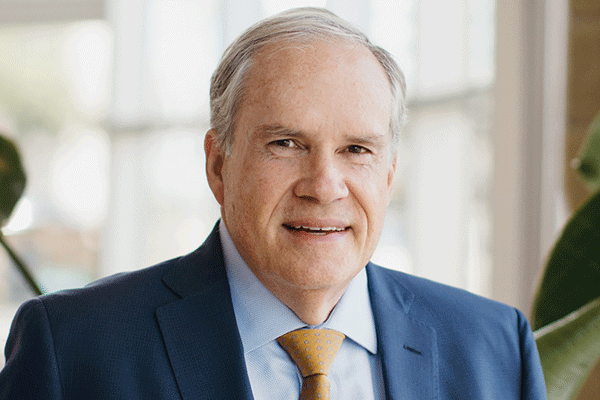 Portrait of a middle-aged man in a navy suit and yellow tie, smiling in a bright office setting.