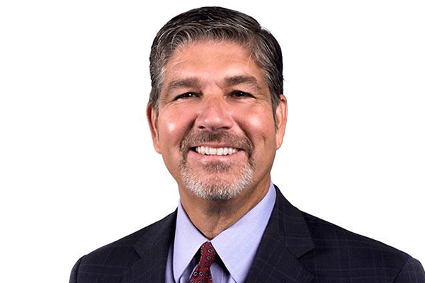 Head-and-shoulders portrait of a smiling man in a dark suit and red tie against a white background, a professional business headshot.