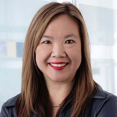 Winjie Miao - Texas Hospital Association Portrait of a smiling woman with shoulder-length brown hair, wearing a dark blue blouse, in a bright office setting.