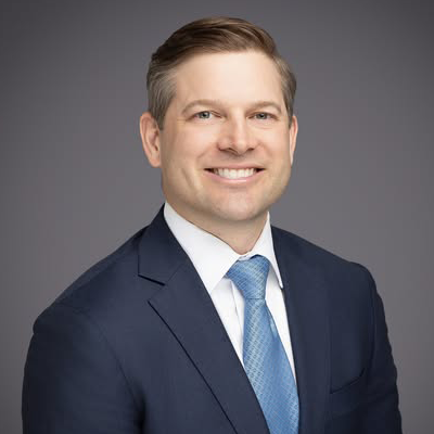 Howard Garner - Texas Hospital Association Professional headshot of a smiling man in a navy suit and light blue tie against a gray background.