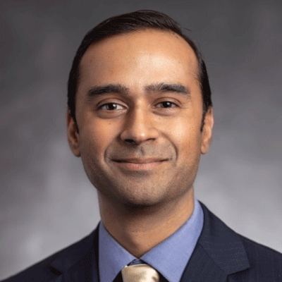 Arabinda "Ara" Pani - Texas Hospital Association Professional headshot of a man in a navy suit and light blue shirt, beige tie, smiling at the camera.