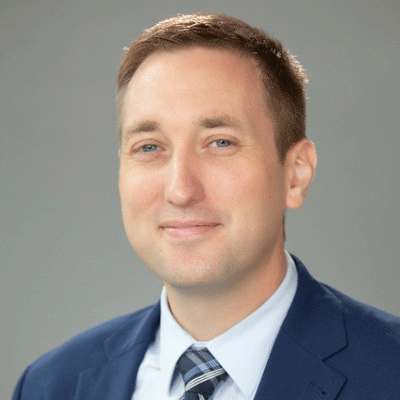 David Matteson - Texas Hospital Association Professional headshot of a man in a blue suit and striped tie against a neutral gray background.