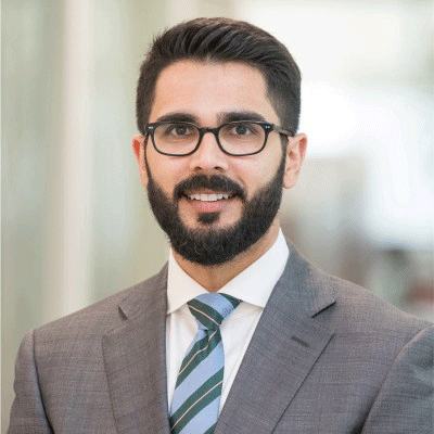 Raza Rashid - Texas Hospital Association Professional headshot of a man with dark hair and a beard wearing glasses, a gray suit, white shirt, and teal striped tie, smiling in an office setting.