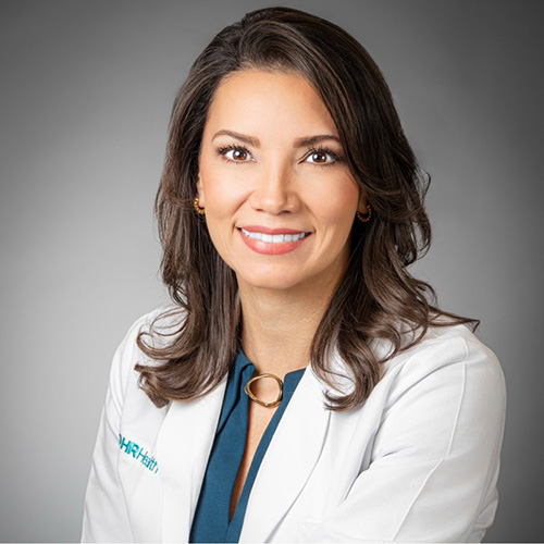 Aida Coronado-Garcia - Texas Hospital Association Portrait of a smiling female doctor in a white coat, facing the camera against a neutral gray background.