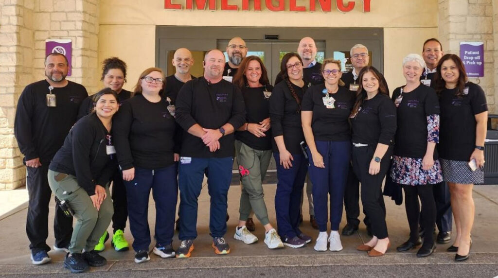 CHRISTUS Santa Rosa Hospital Westover Hills, Bill Aston 2026 Honorable Mention - Texas Hospital Association Group of hospital staff wearing black shirts standing outside the emergency entrance for a team photo.