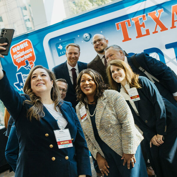 Diverse professionals posing for a selfie at a healthcare event, badges visible, in front of a blue Texas-themed bus.
