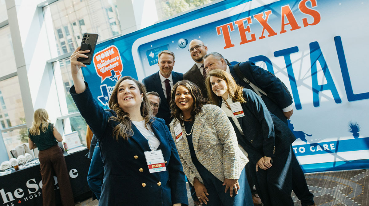 Diverse professionals posing for a selfie at a healthcare event, badges visible, in front of a blue Texas-themed bus.