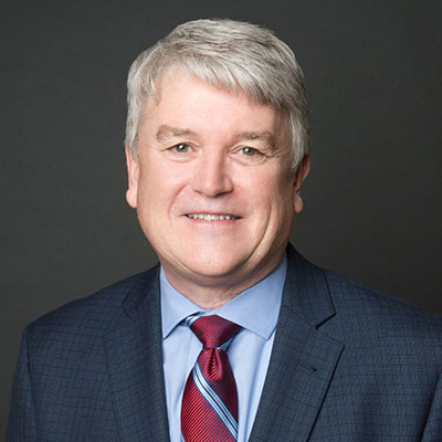 Doug Holzbog - Texas Hospital Association Professional headshot: smiling man in a navy suit and red tie against a dark background