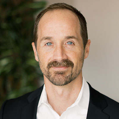 Jon Duckert - Texas Hospital Association Head-and-shoulders portrait of a man with blue eyes and a trimmed beard, wearing a white shirt and black blazer.