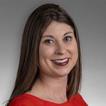 Portrait of a smiling woman with shoulder-length brown hair wearing a red blouse, looking at the camera.