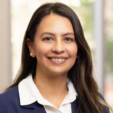 Professional headshot of a smiling woman with long dark hair in a navy blazer and white shirt.