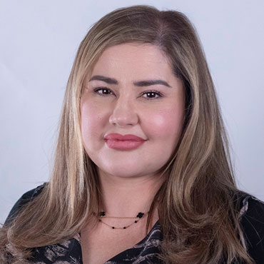 Head-and-shoulders portrait of a woman with long light brown/blonde hair, pink lipstick, wearing a black top and a delicate necklace.